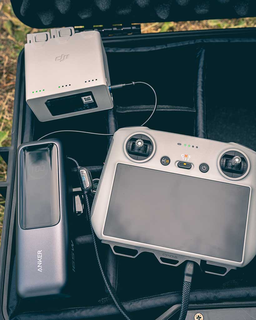 offener Fotokoffer mit Powerbank und Drohnen Fernbedienung beim Laden
